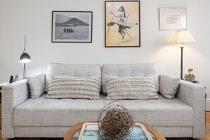 A living room with a grey sofa, two framed pictures, a lamp, and a small plant.