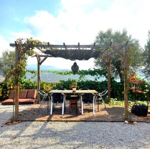 Un espace extérieur aménagé, abrité et doté de tables et de chaises, entouré de verdure et offrant une vue sur le paysage.