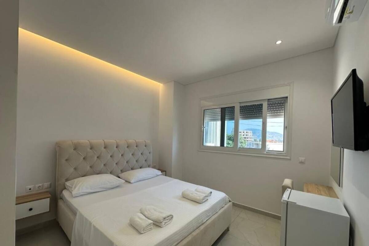 A bedroom with a large bed, a flat-screen TV, a window, and a built-in desk.