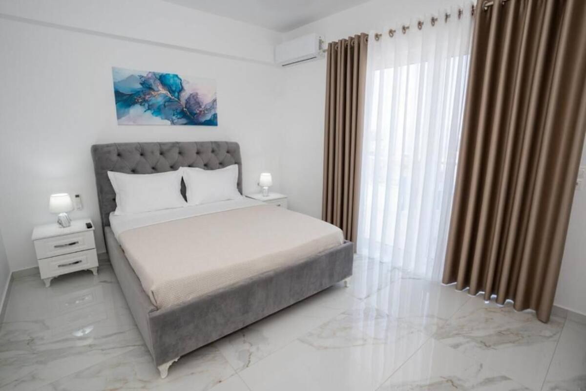 A bedroom with a bed, nightstands, a painting, and curtains.