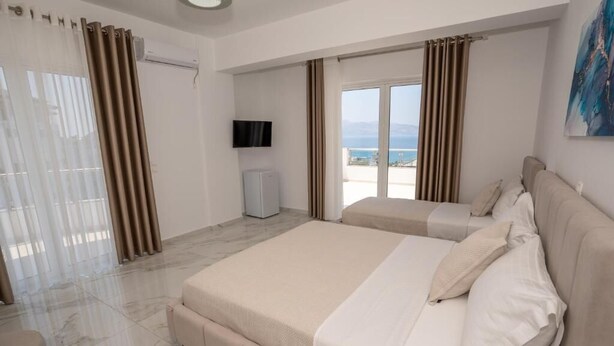 Une chambre d’hôtel avec un lit, une télévision, un balcon avec des rideaux et une vue sur la mer.