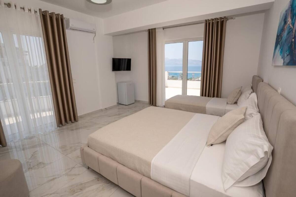 A hotel room with a bed, a TV, a balcony with curtains, and a view of the sea.