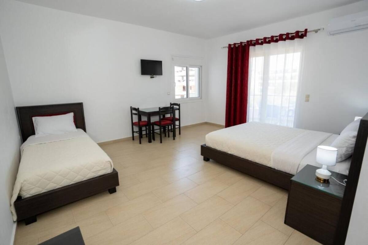 A hotel room with two beds, a desk, a chair, a TV, and a window with curtains.