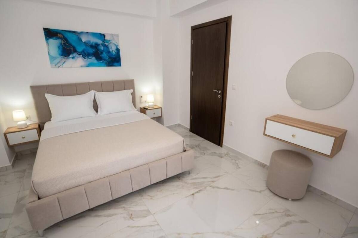 A bedroom with a bed, bedside tables, a door, a round mirror, and a wall-mounted shelf.