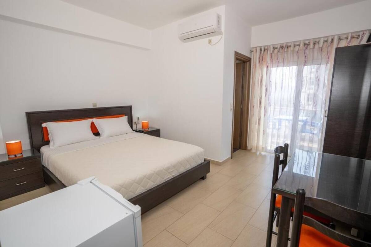 A hotel room with a bed, a desk, a chair, a TV, and an air conditioning unit.
