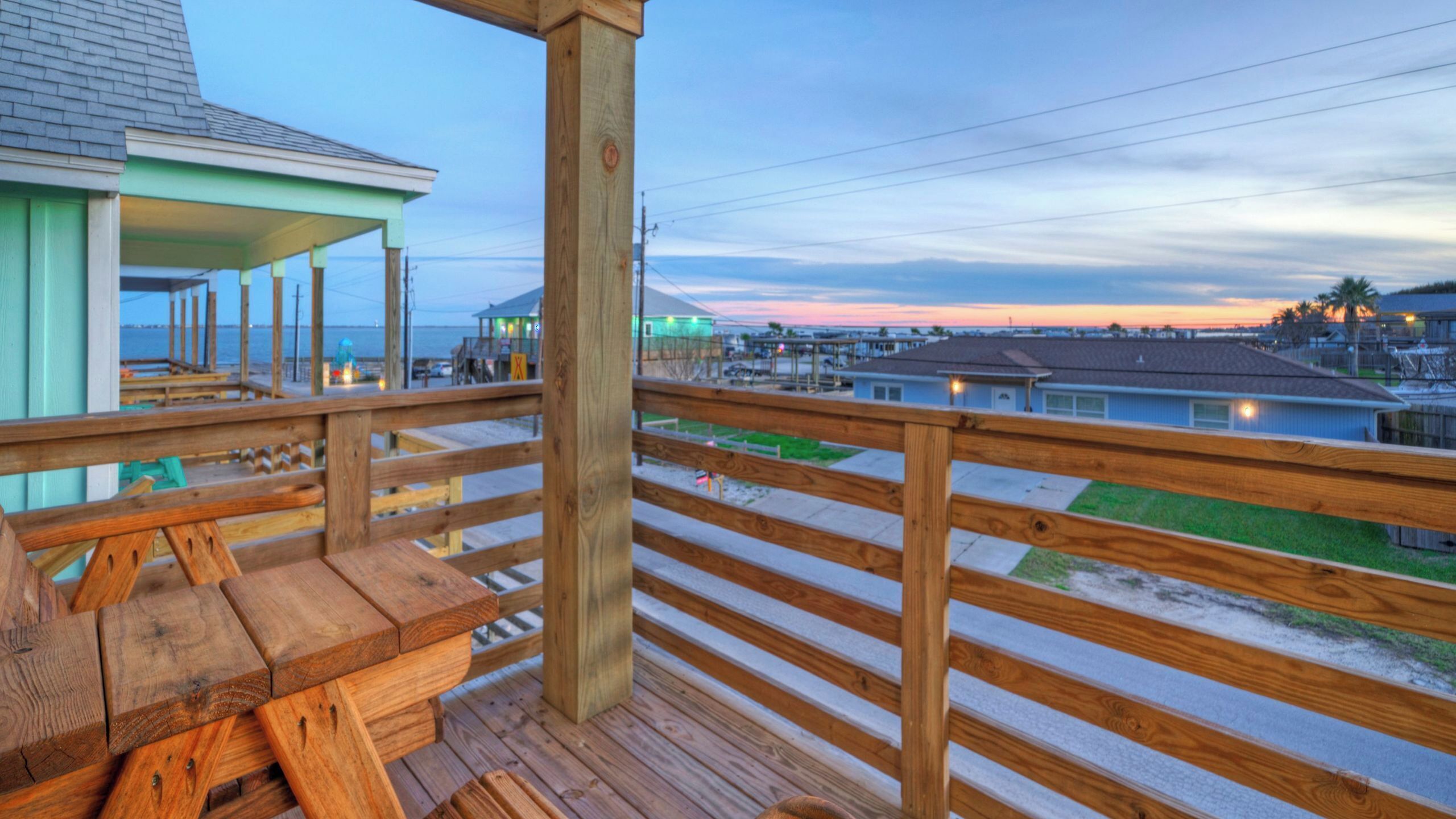 Um deck de madeira com um banco, com vista para uma área residencial com casas e uma praia.
