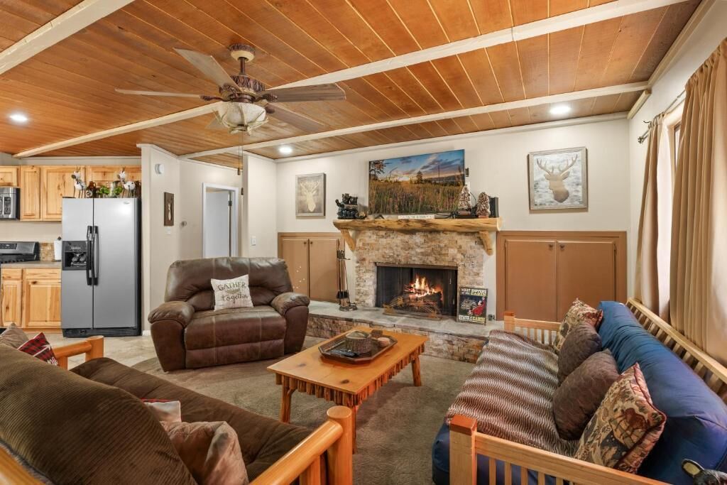Una sala de estar con chimenea, sofás de cuero, una mesita de centro y un ventilador de techo.