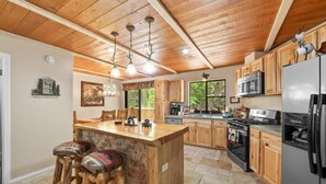 Une cuisine avec des meubles de rangement en bois, un îlot central doté de tabourets, un réfrigérateur et une cuisinière.