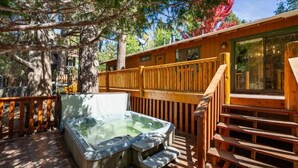 Een hottub in een houten terrasgedeelte met een houten reling en een trap naar een gebouw.