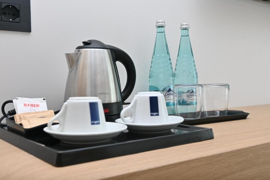 A coffee station with a kettle, cups, glasses, and water bottles.