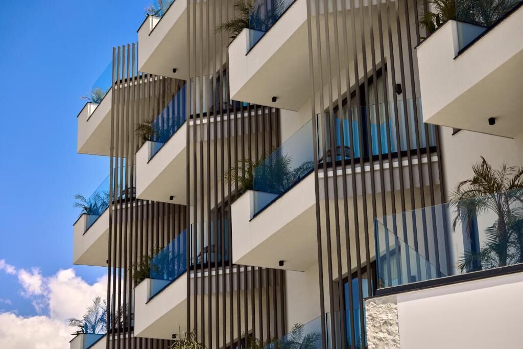 Un immeuble moderne à plusieurs étages, doté de balcons, de grandes fenêtres et de quelques éléments de verdure.