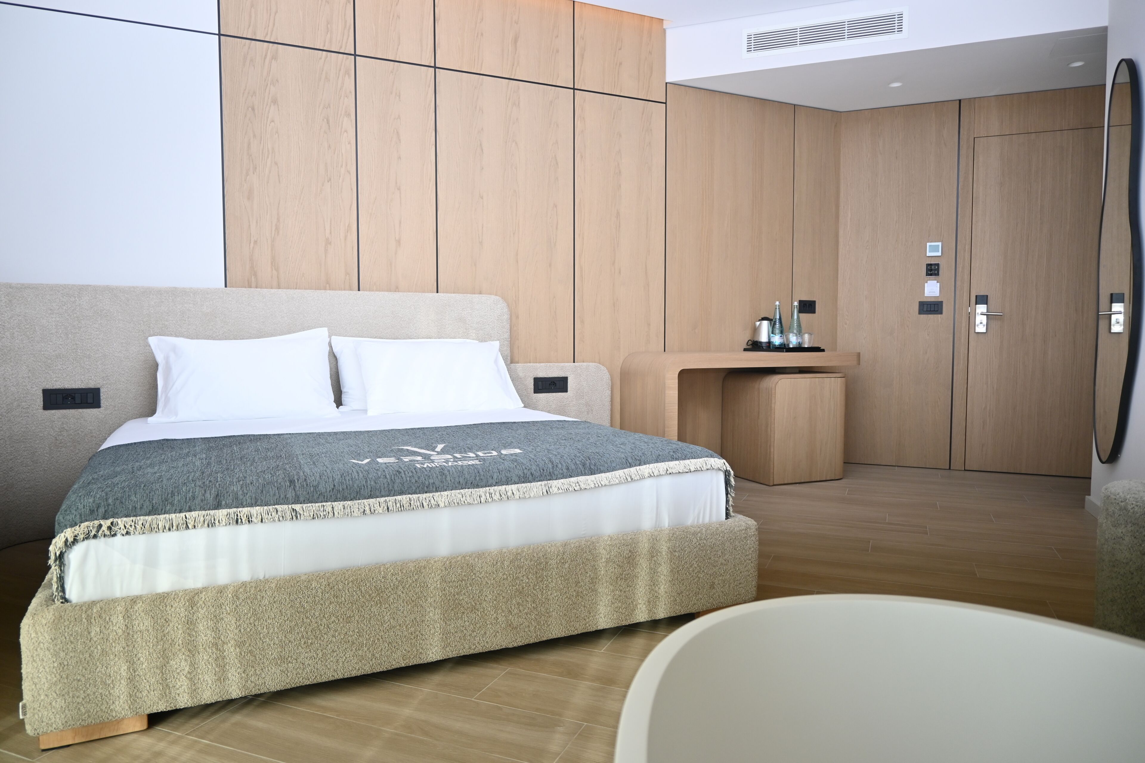 Un dormitorio moderno con una cama grande, paredes de paneles de madera, una mesita de noche y un espejo.