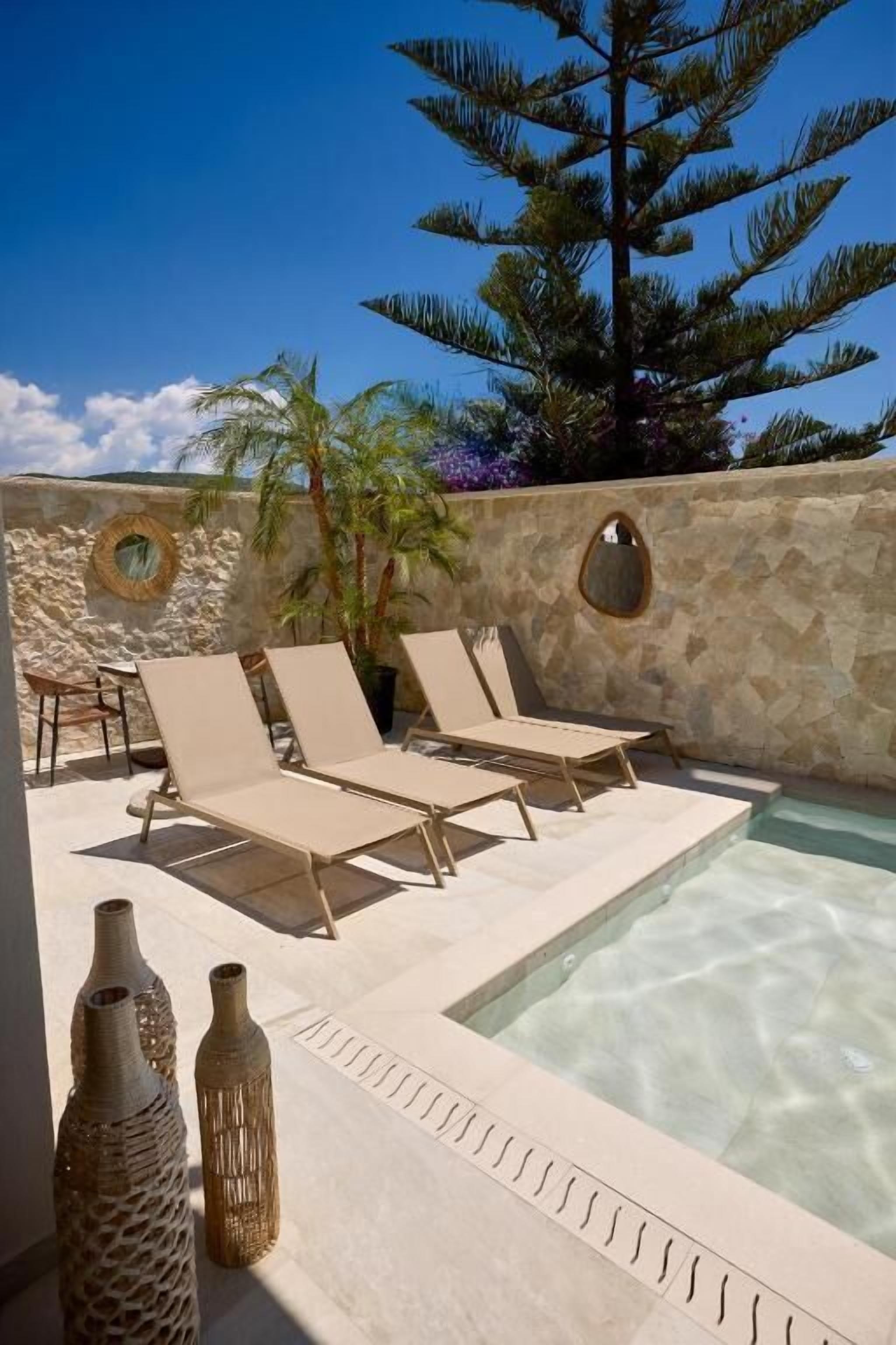 A pool area with lounge chairs, decorative vases, and a stone wall with circular cutouts.