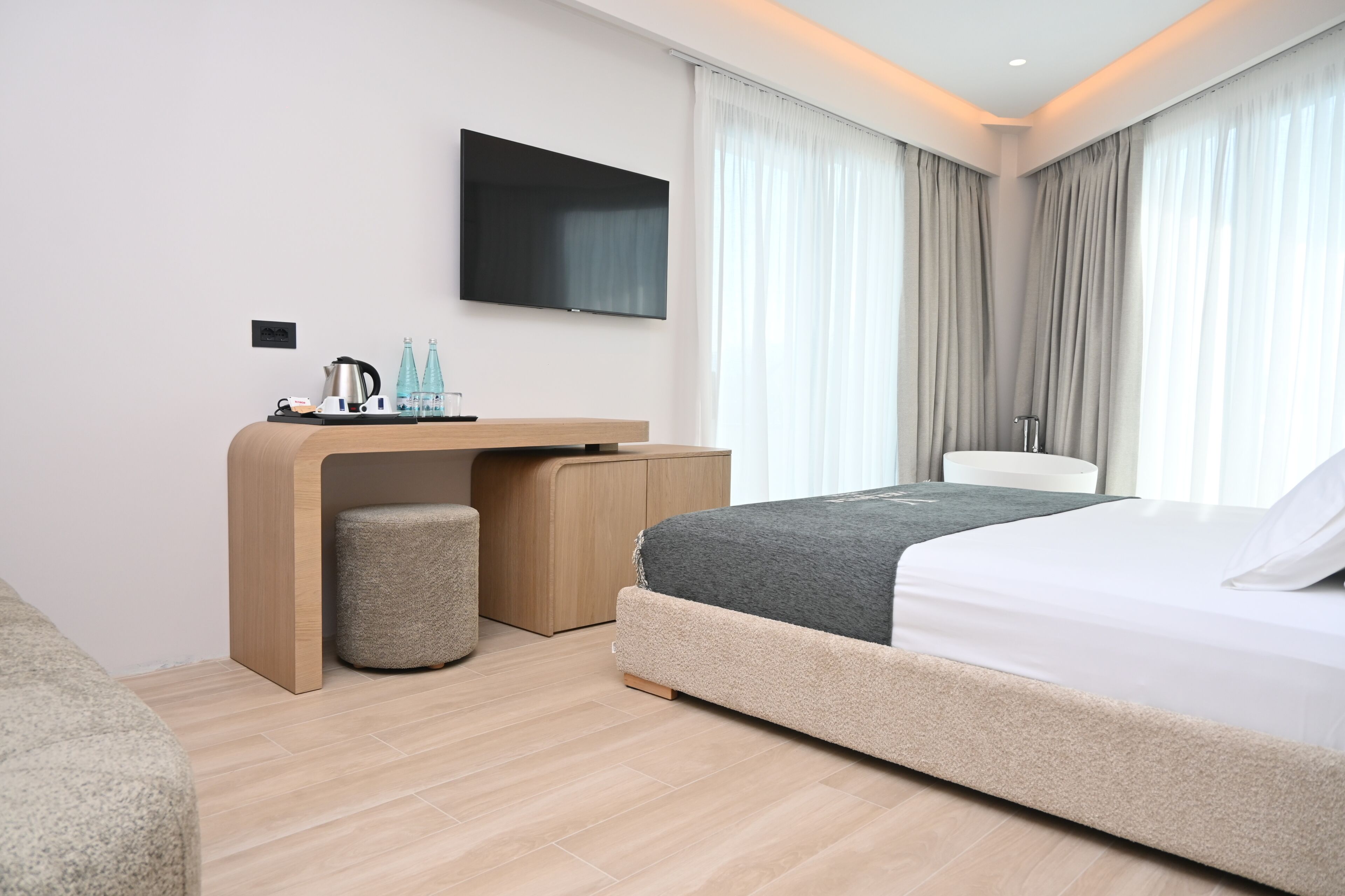 Una habitación de hotel moderna con cama, escritorio, silla, televisión y ventana con cortinas.