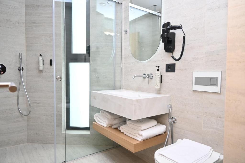 A modern bathroom with a glass shower enclosure, a white sink, and a towel rack.