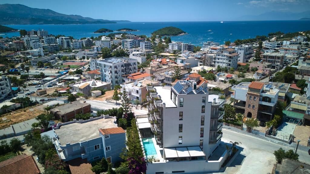 Une zone urbaine côtière où se côtoient des immeubles résidentiels et commerciaux, avec un bâtiment blanc remarquable surmonté d’une piscine sur le toit, et offrant une vue sur la mer.