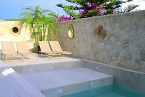 Un área de piscina con sillones de descanso, una pared de piedra y elementos decorativos.