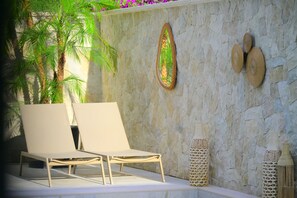 Una pared de piedra con un espejo, dos sillones y jarrones decorativos.
