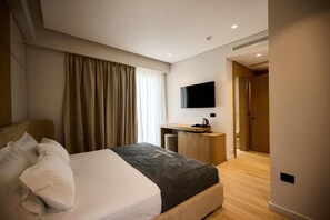 Una habitación de hotel con una cama, un escritorio, un televisor y una puerta que da a otra habitación.