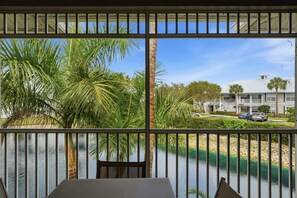 Ein Balkon mit Blick auf einen Fluss, Palmen und ein Gebäude mit parkenden Autos.