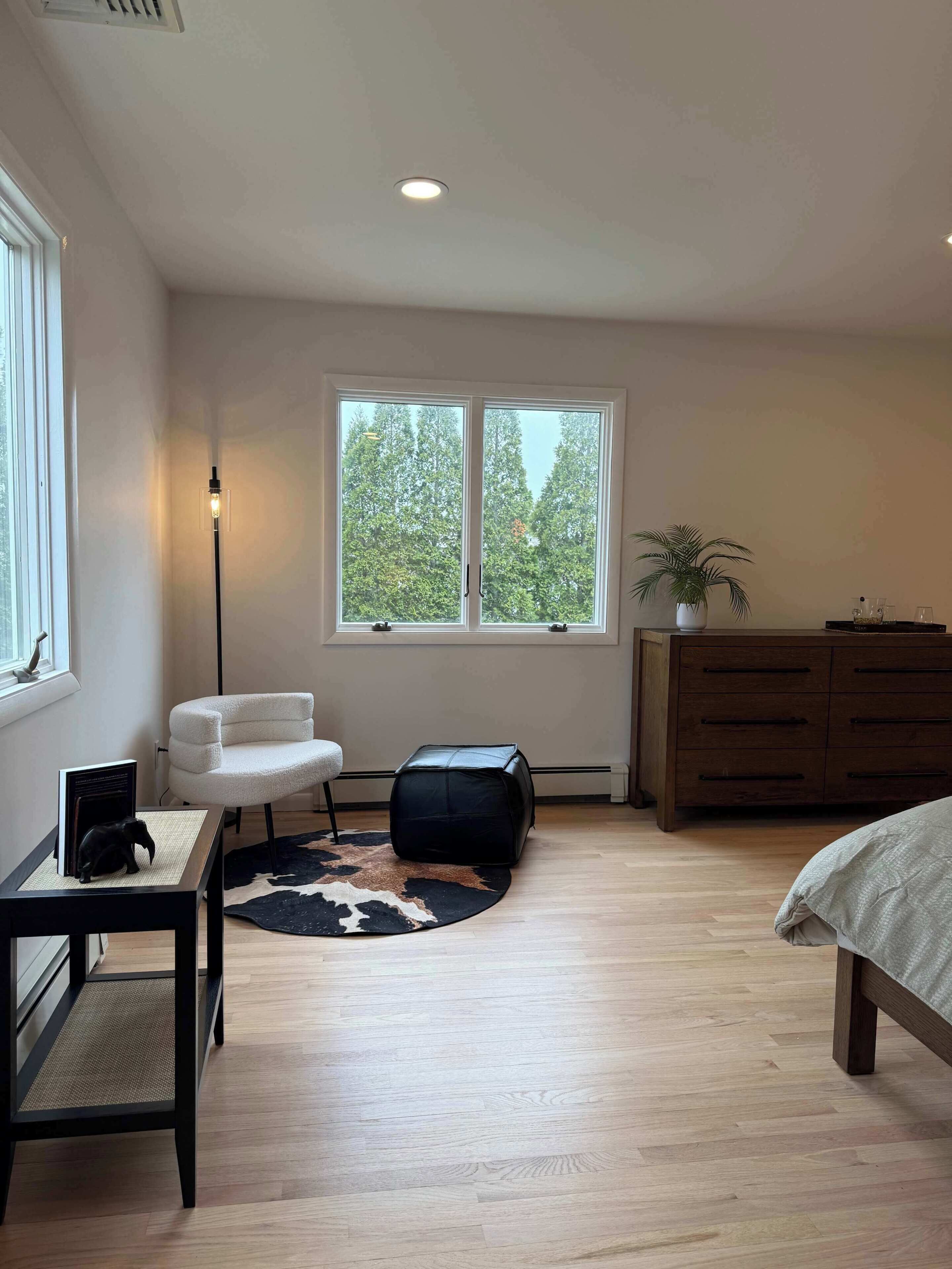 Une chambre à coucher avec un lit, un bureau et une chaise, une fenêtre donnant sur des arbres, une commode et une plante en pot.