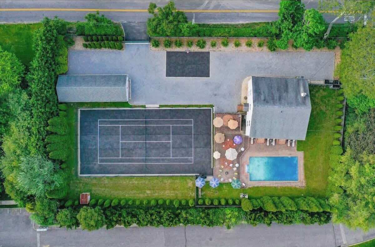 An aerial view of a property with a tennis court, a swimming pool, and a patio area with outdoor furniture.