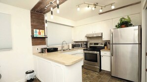Una cucina moderna con mobili bianchi, elettrodomestici in acciaio inossidabile, un'isola centrale e una lampada a sospensione.