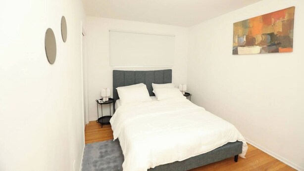 Una camera da letto con un letto, comodini, una finestra con tende e un quadro appeso al muro.