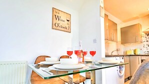 Un coin repas avec une table en verre, des chaises et une bouteille de vin.