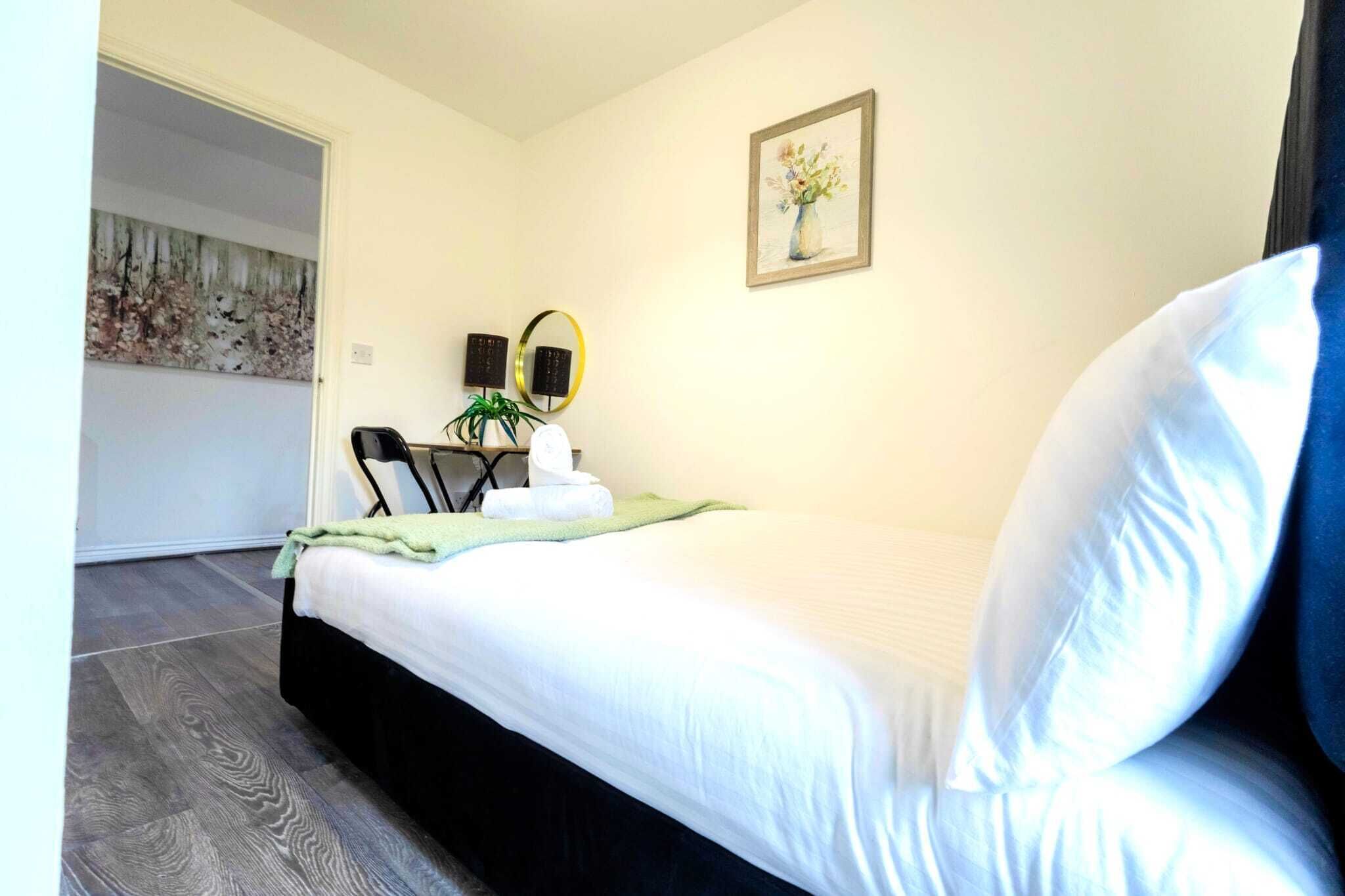 Een hotelkamer met een bed, een stoel, een bureau met een plant, een schilderij en een ingelijste foto aan de muur.