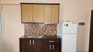 A kitchen with wooden cabinets, a tiled backsplash, a sink, and a white refrigerator. - Hotel Studio Eno Ksamil (Ksamil)