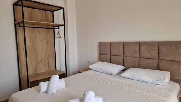 A hotel room with a large bed, two pillows, a headboard, a wooden shelf unit, and neatly folded towels. - Hotel Studio Eno Ksamil (Ksamil)