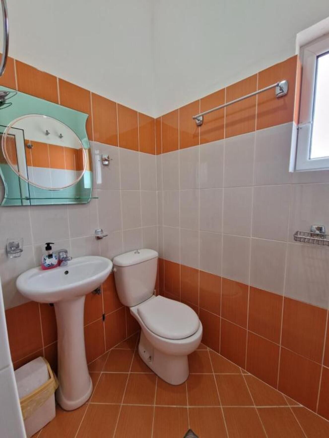 A bathroom with a pedestal sink, toilet, and a mirror with a round frame.