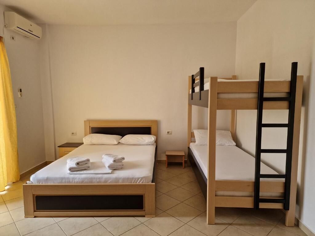 A room with a single bed, a bunk bed, a small table, and an air conditioning unit.