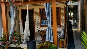 A small house with a tiled roof, a wooden door, and a garden with plants and a hammock. - Beach House Suítes Jeri (Jijoca de Jericoacoara)