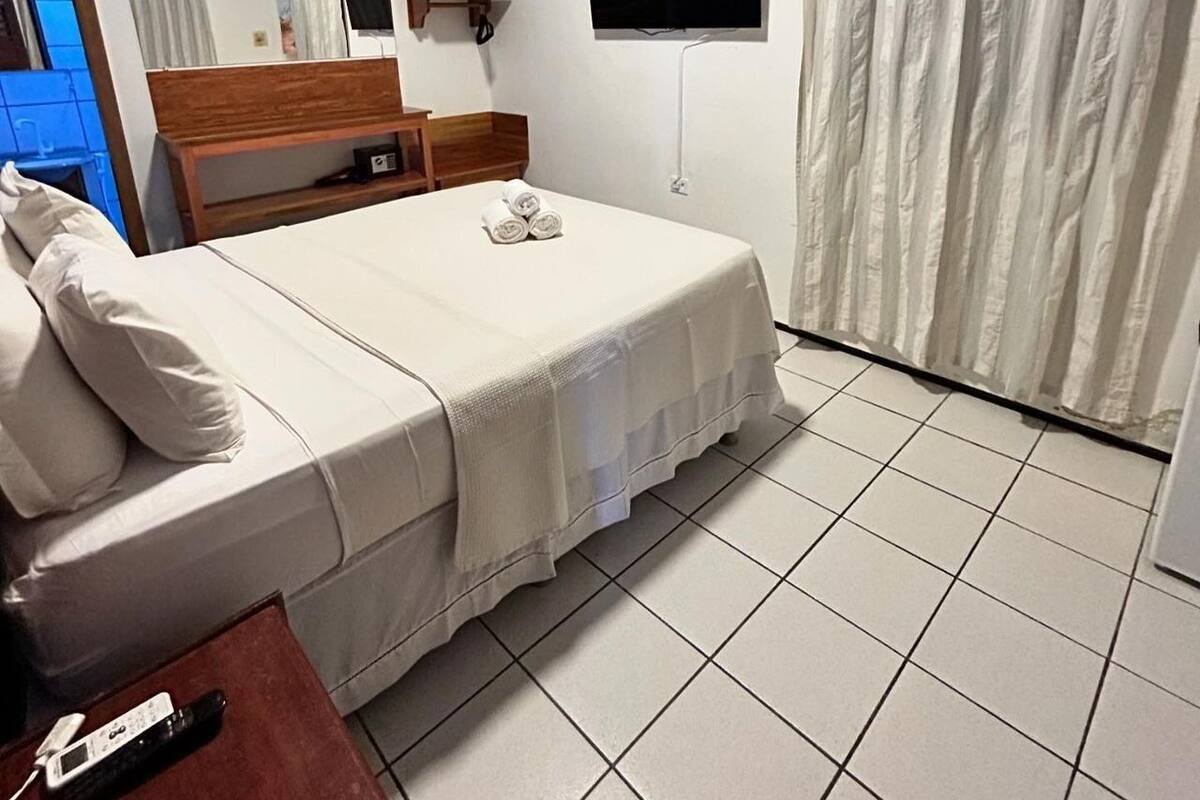 A hotel room with a bed, a TV mounted on the wall, a mirror, and a window with curtains.