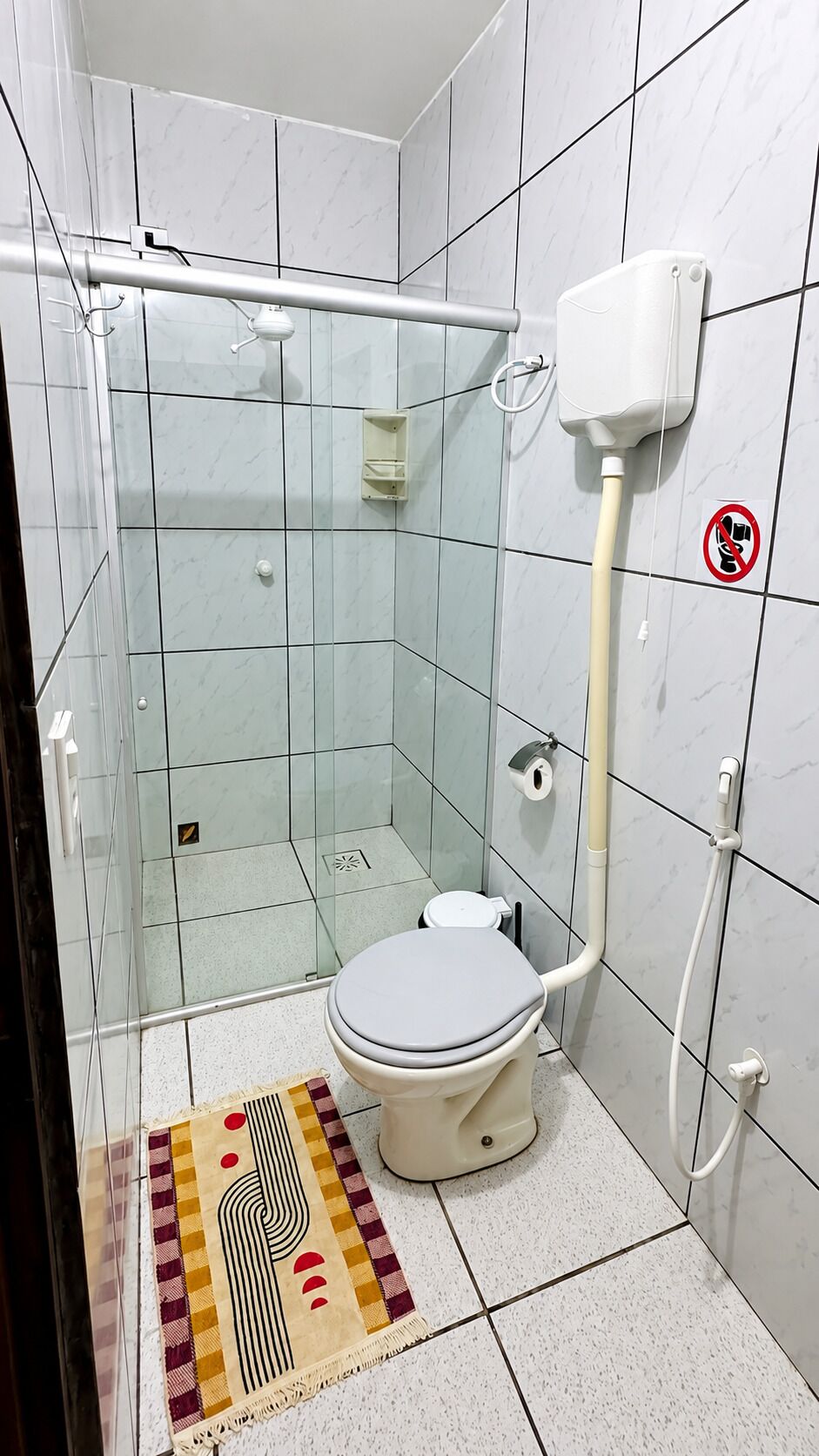 Une salle de bain équipée d’une douche à parois de verre, de toilettes, d’un sèche-mains et d’un panneau indiquant qu’il est interdit de fumer.