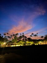 Vista nocturna de una playa con palmeras y un cielo al atardecer.