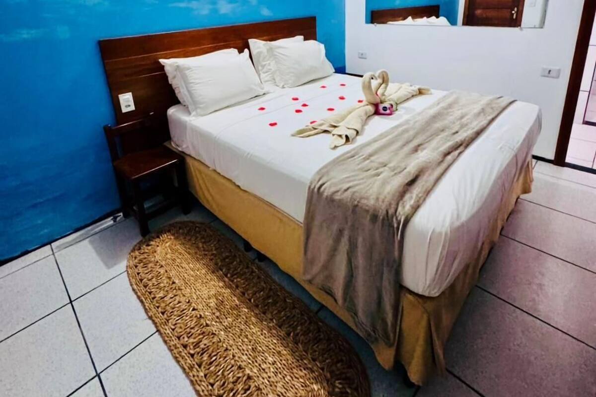 A bedroom with a bed, a nightstand, a woven rug, a blue wall, and a painting.