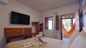 A hotel room with a bed, a TV, a wooden headboard, a desk, and a window with curtains. - Beach House Suítes Jeri (Jijoca de Jericoacoara)