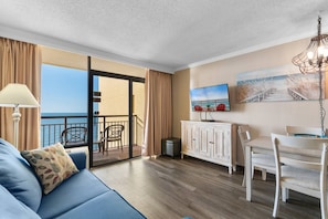 Ein Hotelzimmer mit Balkon, einer Couch, einem Esstisch und einem Fernseher.
