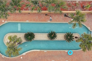 Ein Schwimmbecken mit gefliestem Sonnendeck, umgeben von Palmen und einem Pflasterweg.