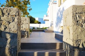 Un chemin de pierres mène à un bâtiment aux murs blancs, sous un ciel d’un bleu limpide.