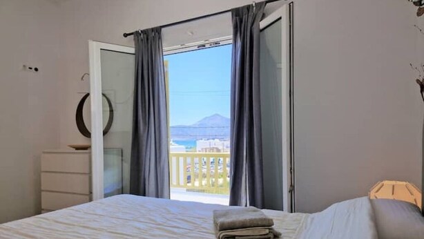 Une chambre à coucher comprenant un lit, une commode, un miroir rond et un balcon avec vue sur une montagne.