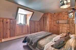 A bedroom with wooden paneling, a bed with striped bedding, a window, and a wall-mounted light fixture.