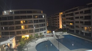A nighttime view of a hotel with a swimming pool, multiple floors, and outdoor seating areas.