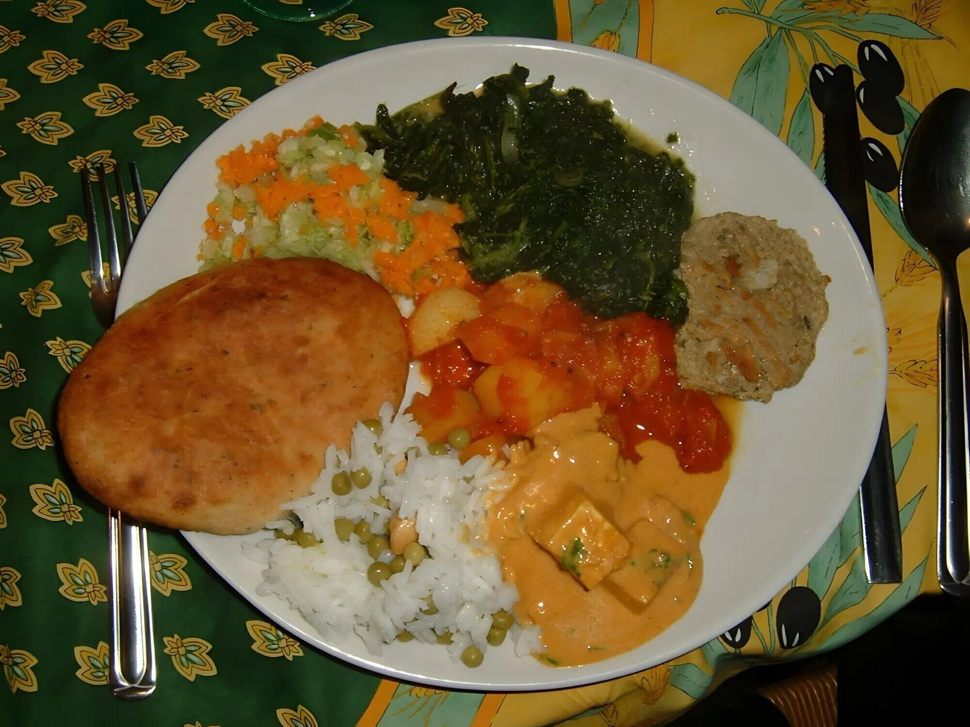Ein Teller mit Reis, Erbsen, Karotten, Blattgemüse und einem Currygericht.