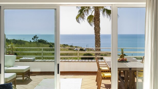 Un balcon avec vue sur la mer, un palmier et une table garnie de fruits.