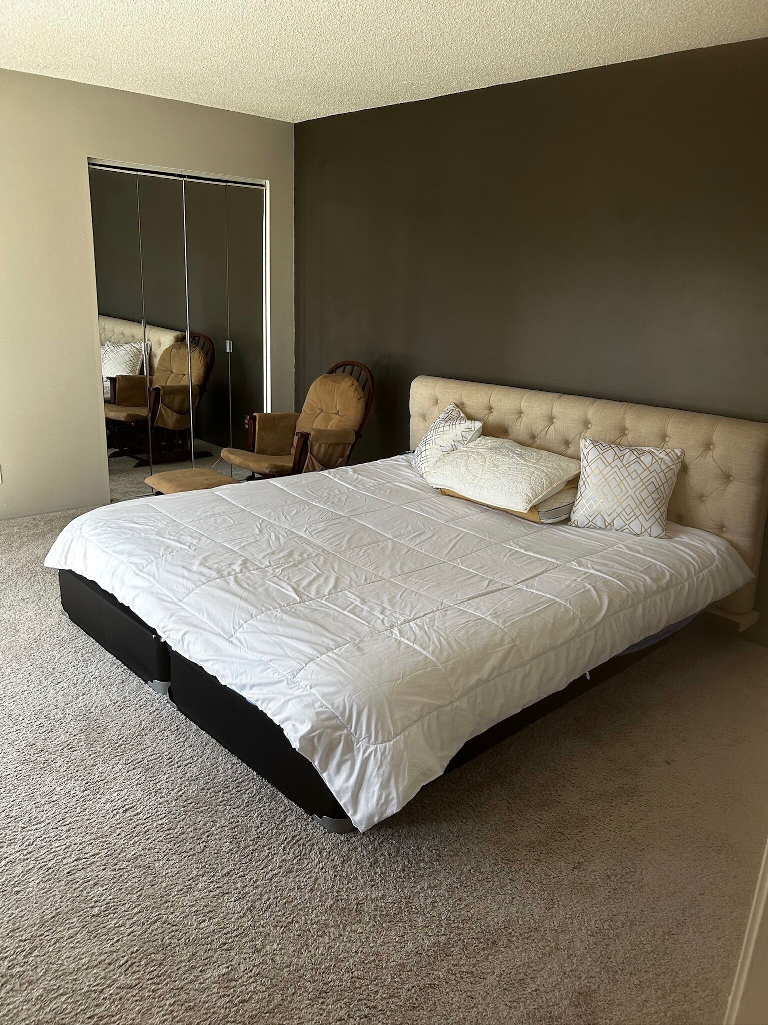 A bedroom with a large bed, a chair, and a mirror.