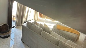 Ett vardagsrum med en soffa, en flätad korg och en utsikt genom ett fönster.